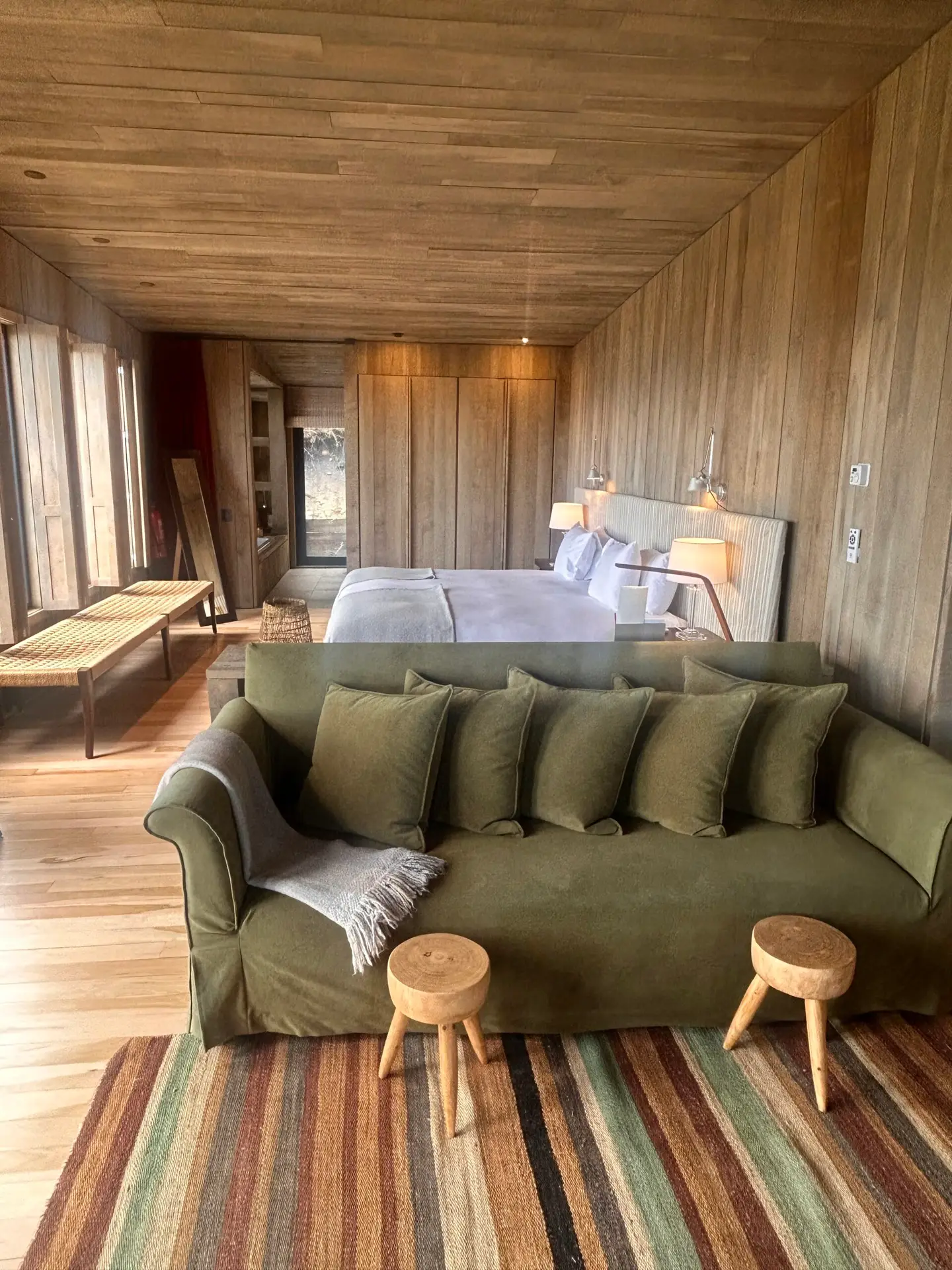 Boutique hotel suite interior with green sofa, natural wood panelling and warm textiles