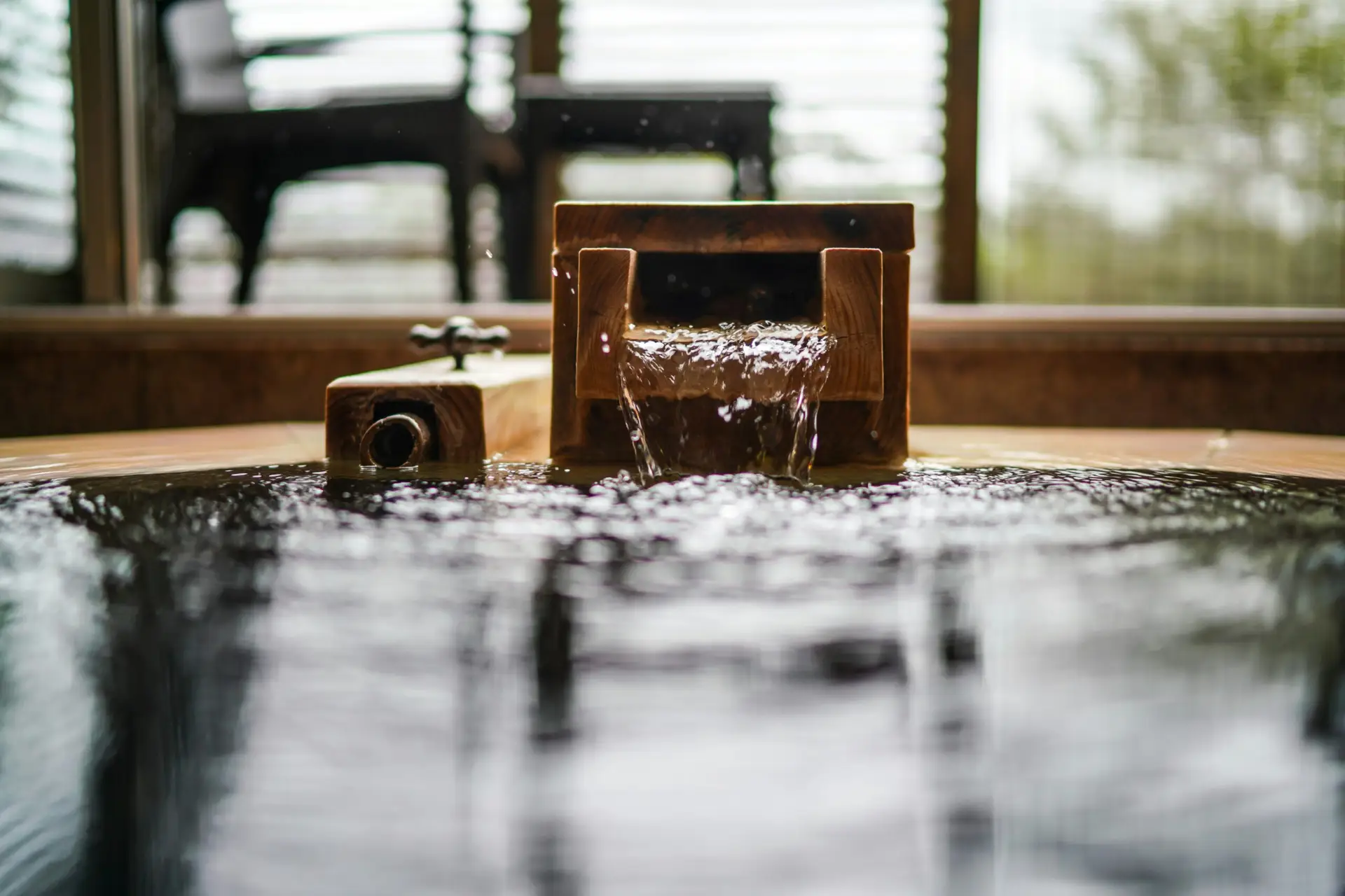 Wooden bath spout pouring water into a soaking tub — natural materials in hotel SPA design